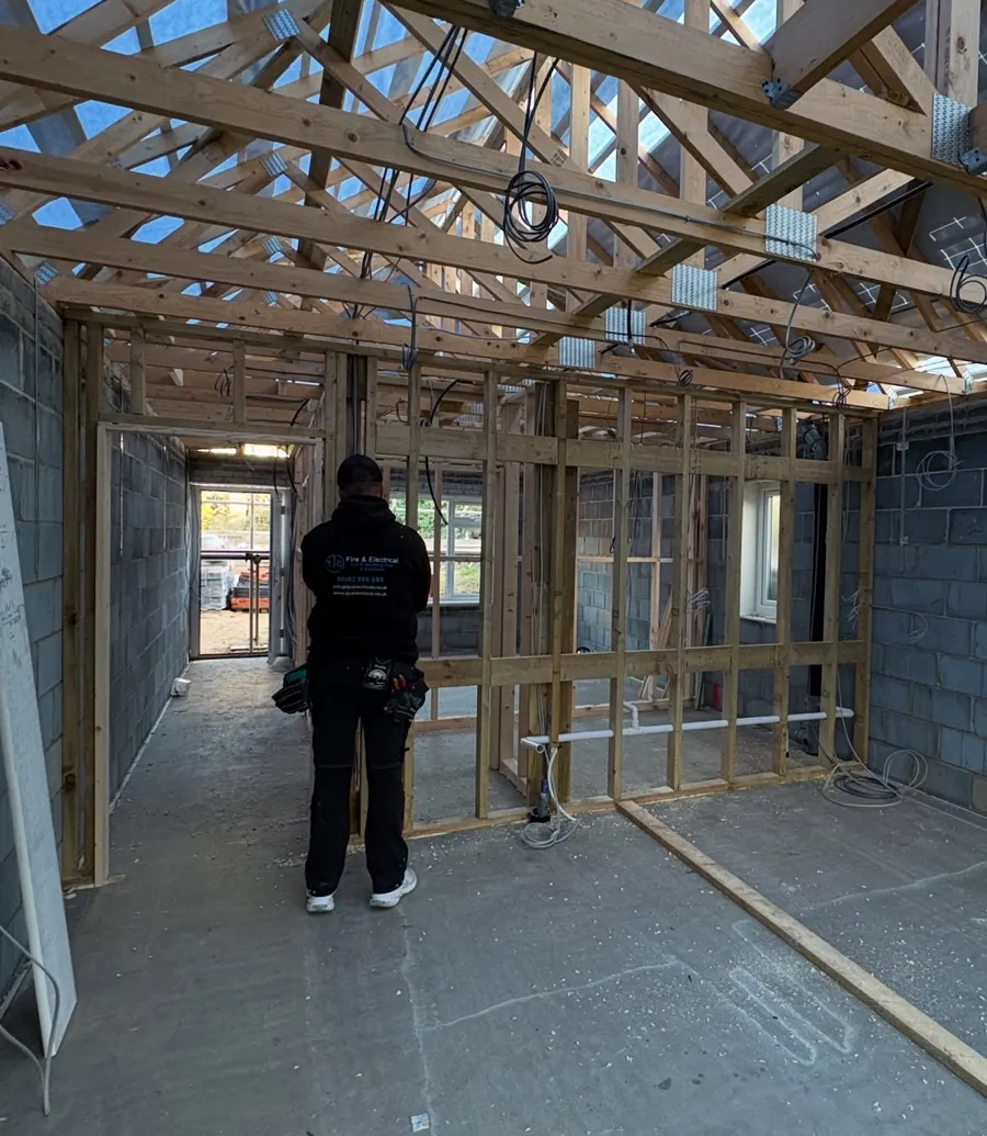 Electrician standing among stud walls and roof trusses during first fix