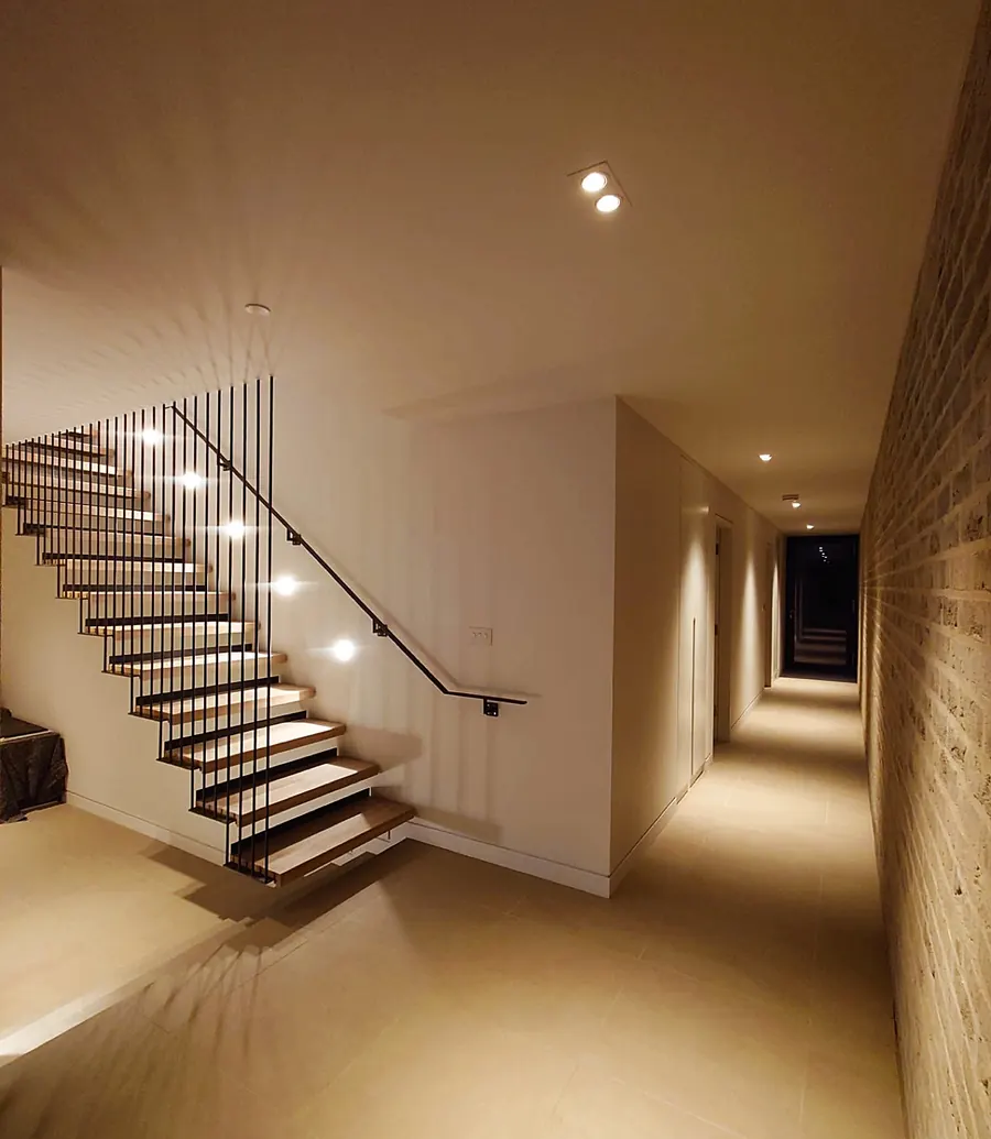 Stairwell and hallway of a home lit by recessed downlights
