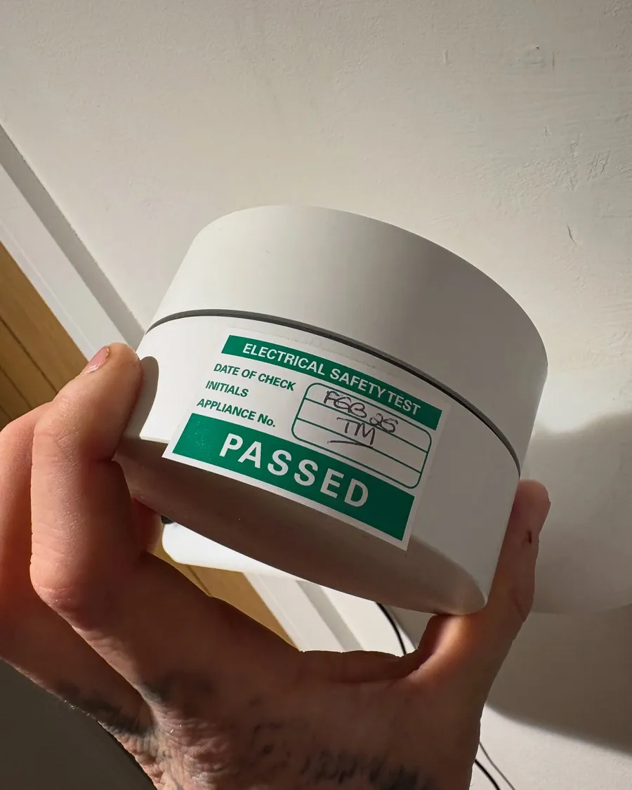 Hand holding a detector head carrying a green PASSED electrical safety sticker