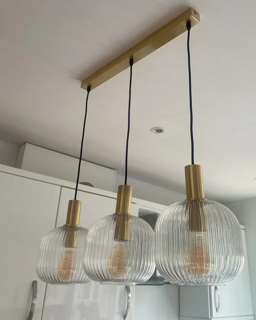 Three ribbed-glass brass pendants hung over a kitchen bar