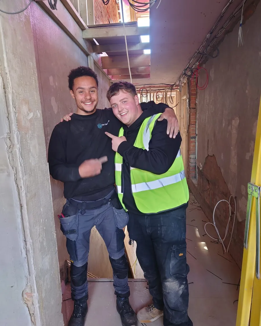 Two apprentices side by side in a corridor mid-fit-out