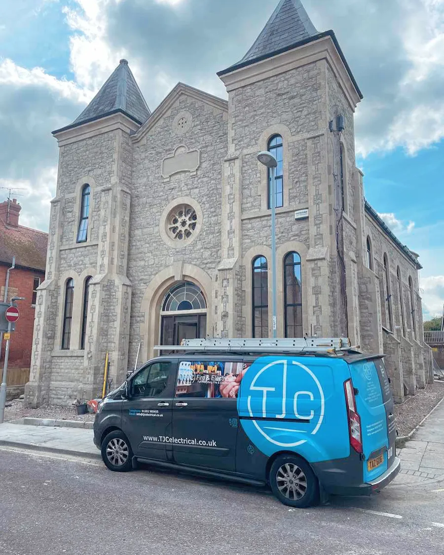 Converted stone church with twin towers, a TJC van parked outside