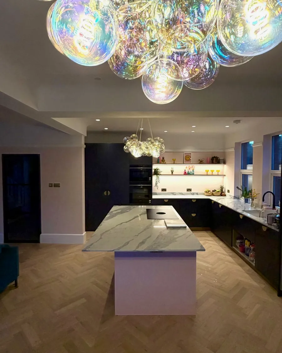 Open-plan kitchen with navy cabinets, marble island and glass bubble chandeliers