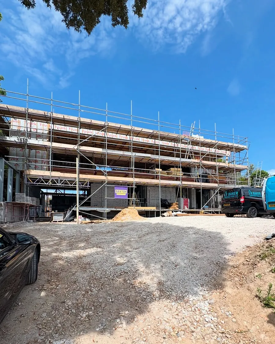 Large new build wrapped in scaffolding under a clear sky