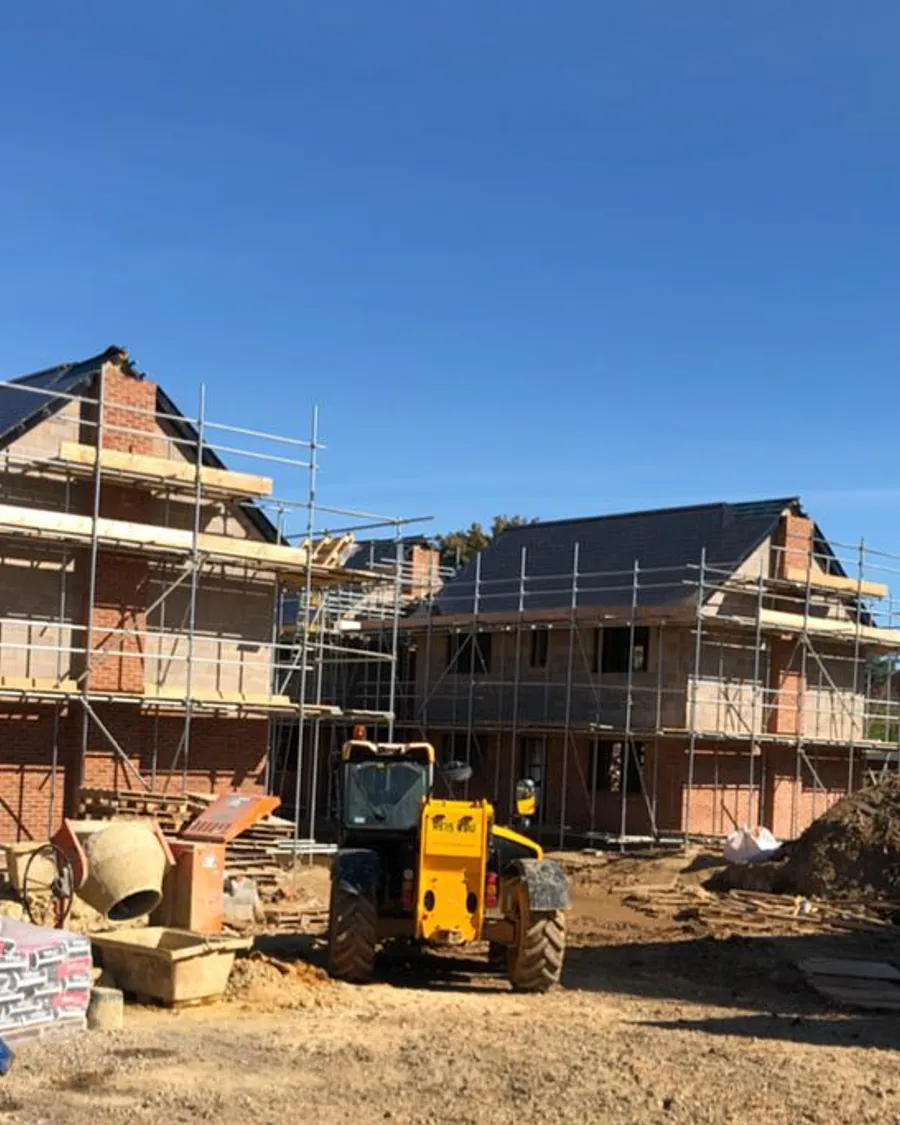 Two scaffolded new-build houses on an active site with a telehandler